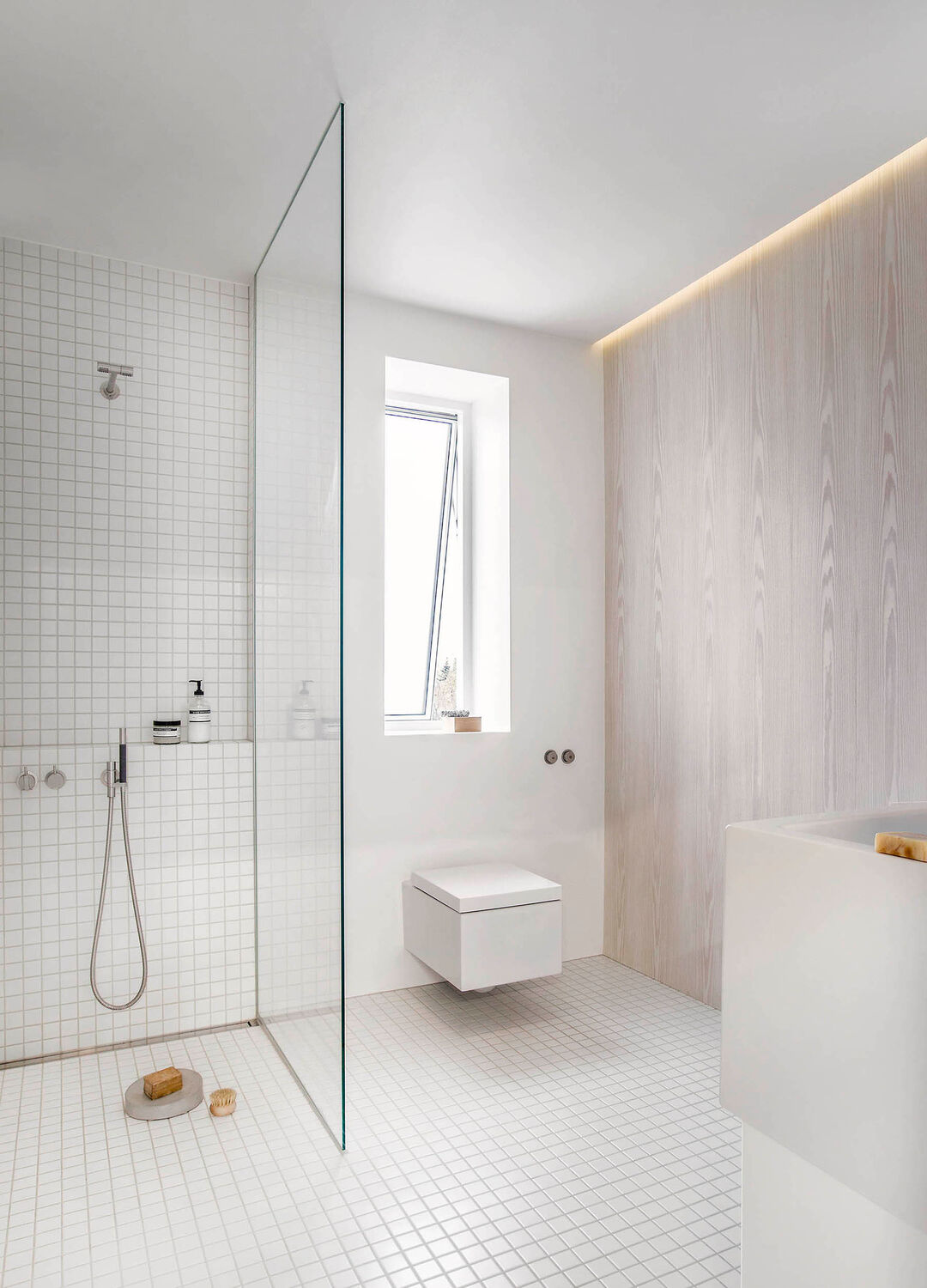 Et funktionelt badeværelse. Væggen er beklædt med hvidpigmenteret Douglas, og sammen med det indbyggede lys, tilføjer væggen en varme og ro til rummet. Vaskeskabet er udført i corian og massiv egetræ.