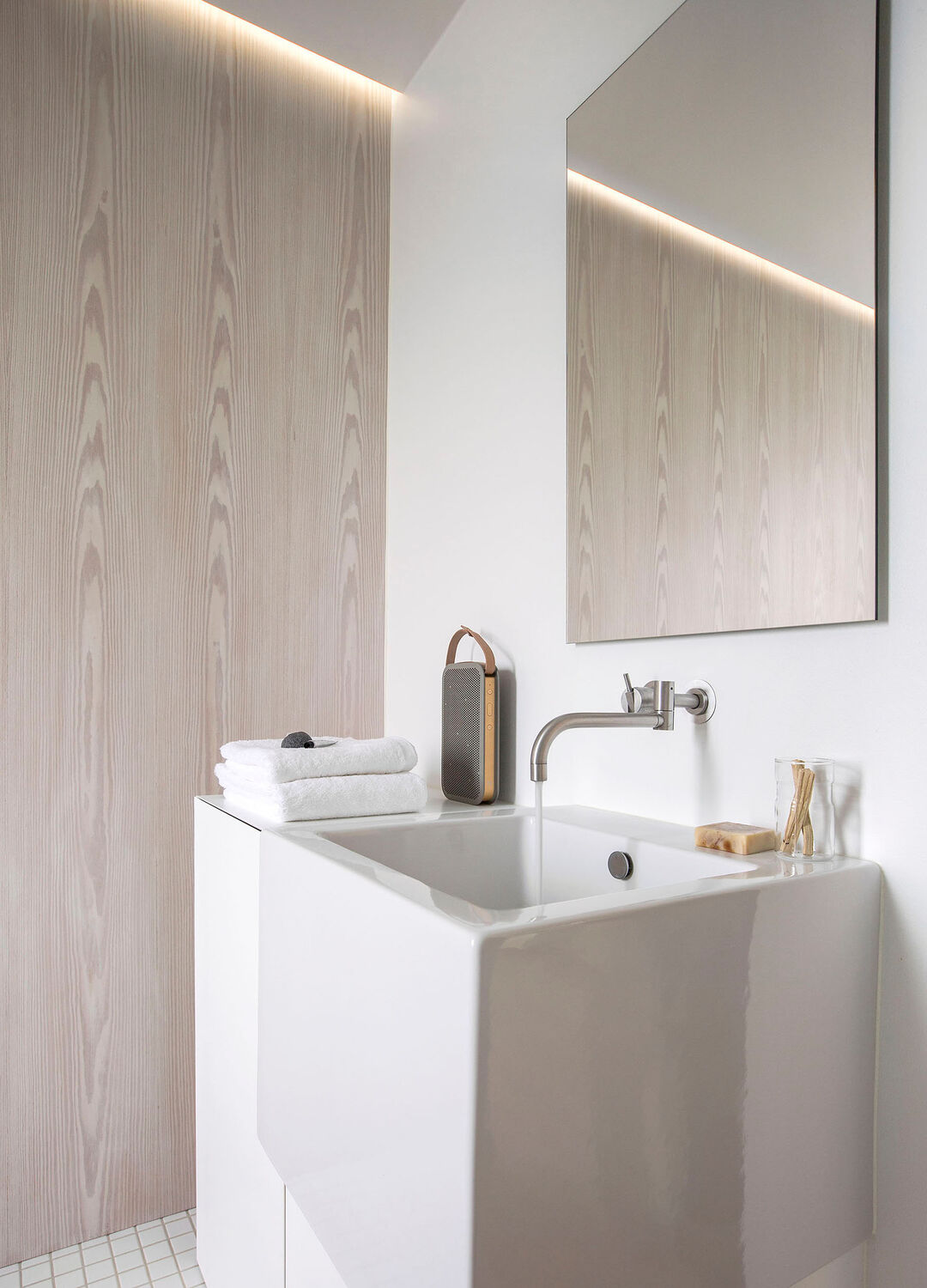 Et funktionelt badeværelse. Væggen er beklædt med hvidpigmenteret Douglas, og sammen med det indbyggede lys, tilføjer væggen en varme og ro til rummet. Vaskeskabet er udført i corian og massiv egetræ.